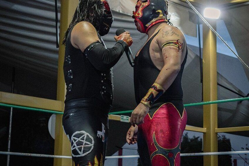 Due wrestler sul ring, con un simbolo a stella sul petto del wrestler a sinistra e una mezzaluna sul petto di quello a destra. 3