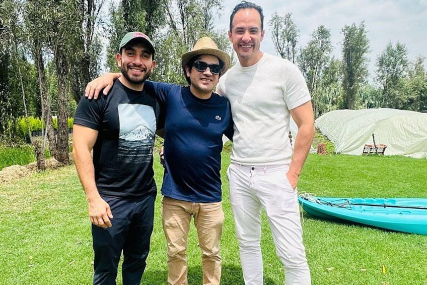 Three people standing outdoors with a tent and a boat in the background. 2