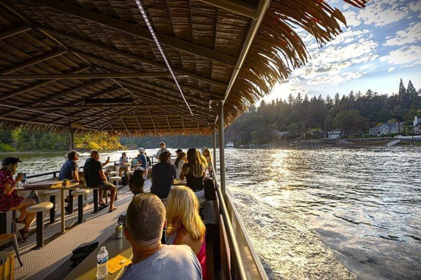 A boat with people dining, a river, and a forested hillside in the background. 2