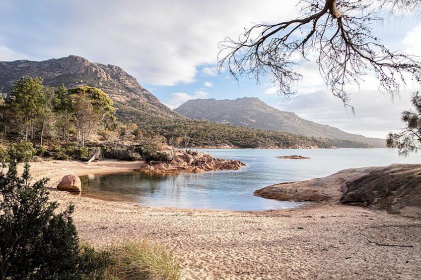 Un paysage côtier avec une plage, une eau calme, des affleurements rocheux et des montagnes en arrière-plan. 3