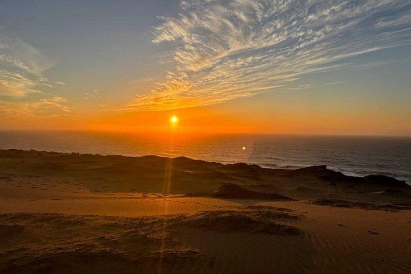 A sunset over a beach with the sun low on the horizon, casting a warm glow over the sand and water. 1