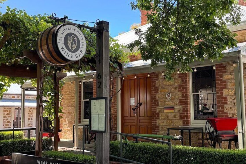 A brick building with a wine bar sign, outdoor seating, and a tree. 4