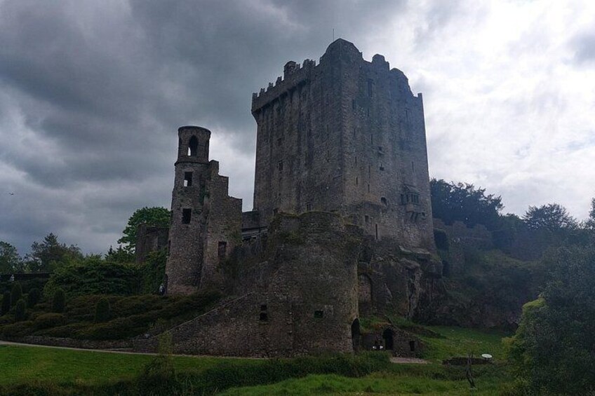 A large, historic castle with a prominent tower, surrounded by lush greenery and a cloudy sky. 4