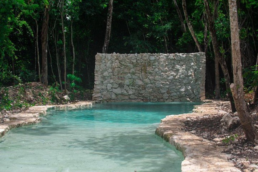 Una piscina natural con agua turquesa cristalina, rodeada de un muro de piedra y un bosque denso. 4