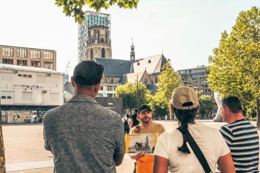 Un grupo de personas de pie al aire libre, un edificio con una torre de reloj y un árbol. 2