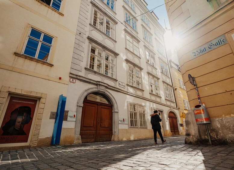 Una calle empedrada con un edificio que tiene una puerta de madera grande y un cartel de Mozart. 1