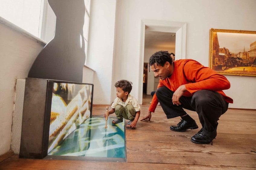Una persona se agacha junto a un niño para observar una obra de arte grande y colorida sobre una mesa de vidrio. 3
