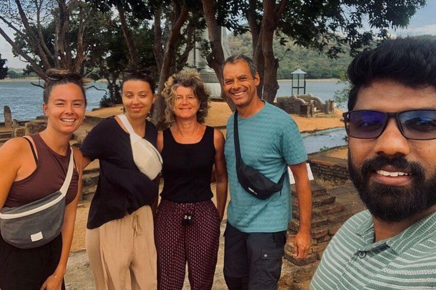 A group of people standing by a body of water with trees and a stone structure in the background. 2