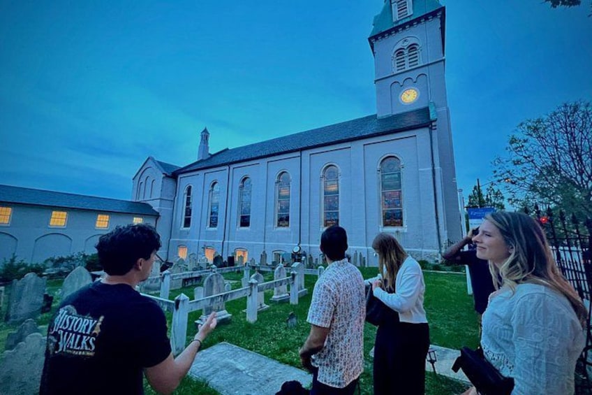 A group of people standing in front of a church with a clock tower. 1