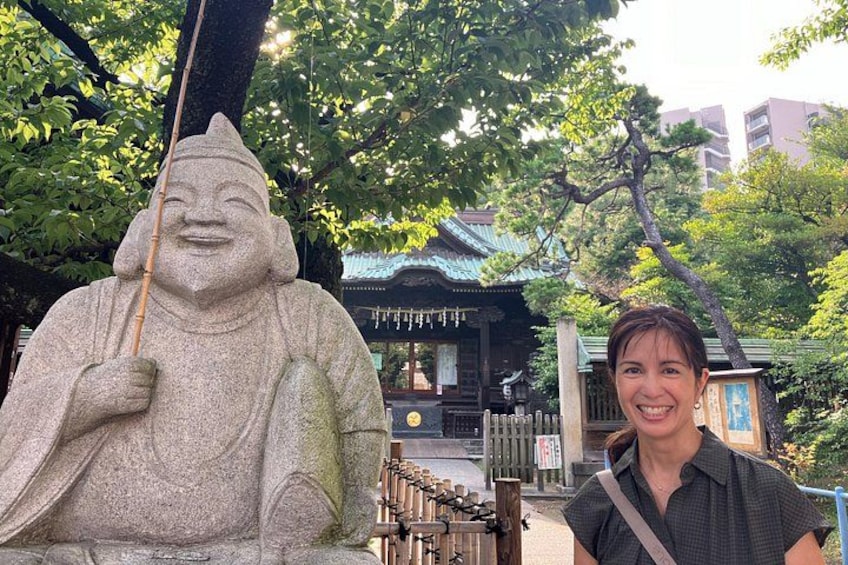 En stenhugget figur med en stav, en traditionel japansk bygning med et flis tag, og en person foran statuen. 3