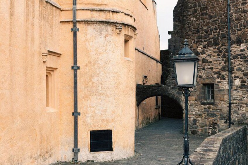 A narrow cobblestone street with a stone bridge, a lamp post, and a building with a rounded corner. 5