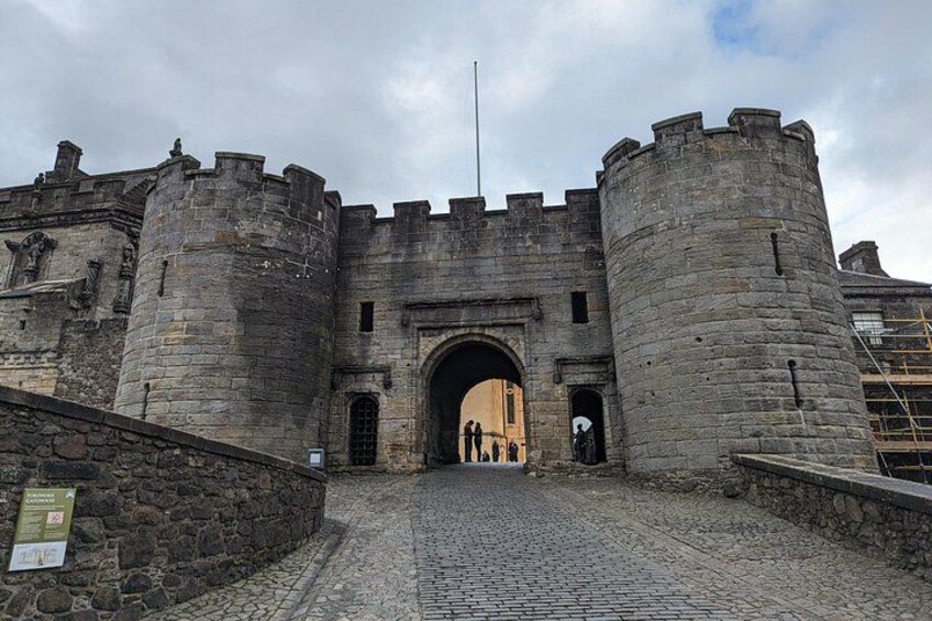 A historic stone castle entrance with a cobblestone pathway leading to a large archway. 2