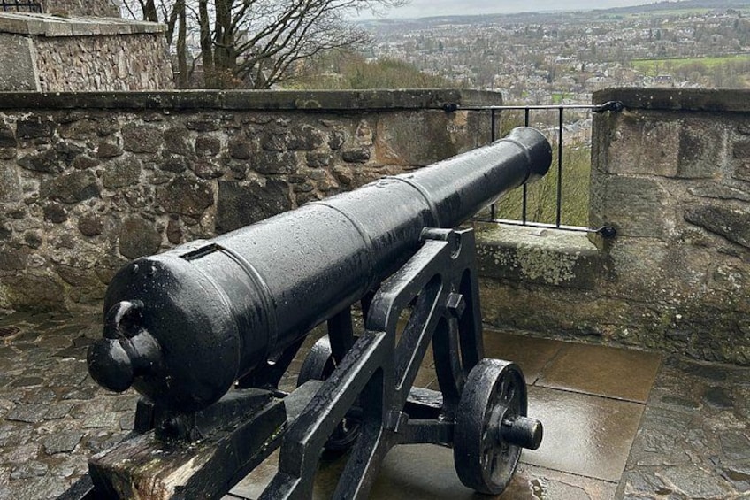 A cannon on a stone platform with a stone wall and a view of a town in the background. 4