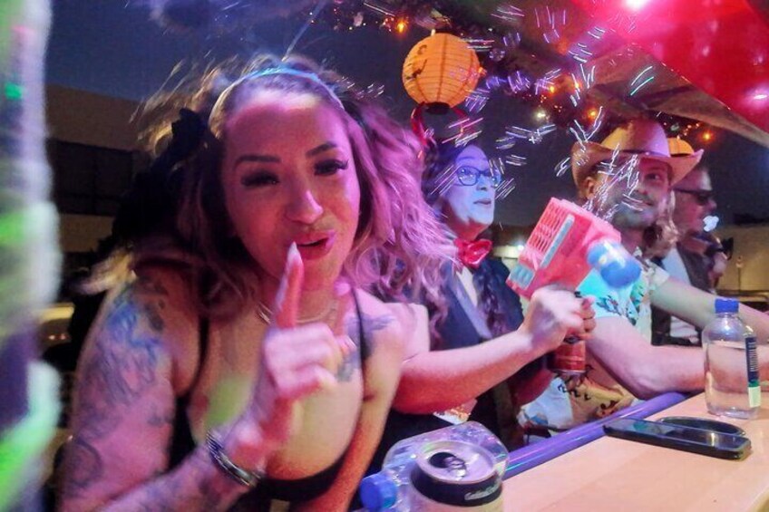 A person with tattoos holding a card, a bottle, and a can on a table. 3