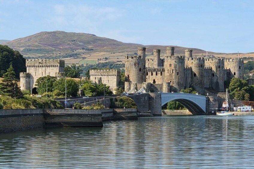 A castle with a bridge over a river, surrounded by greenery and hills. 1