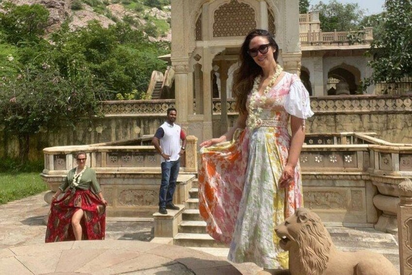 En person i en färgglad klänning som står framför en stenstruktur med trappsteg och en lejonstaty. 4