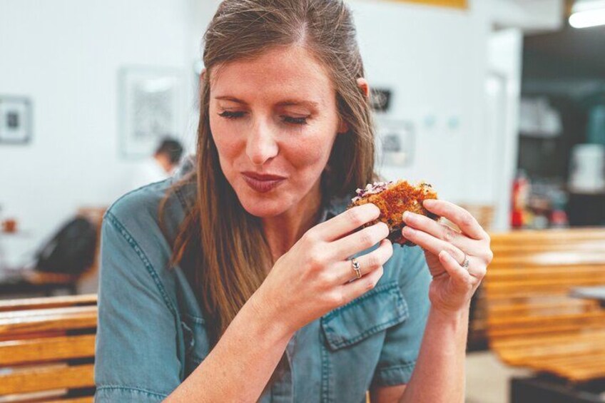 A person sitting at a table in a cafe, holding a piece of food. 5