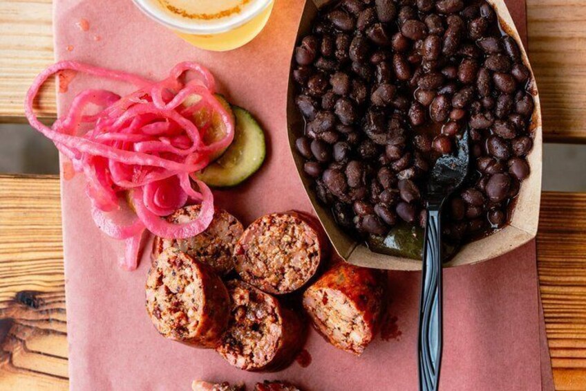 Sliced sausage, black beans, pickled vegetables, and a bowl of sauce on a wooden table. 5