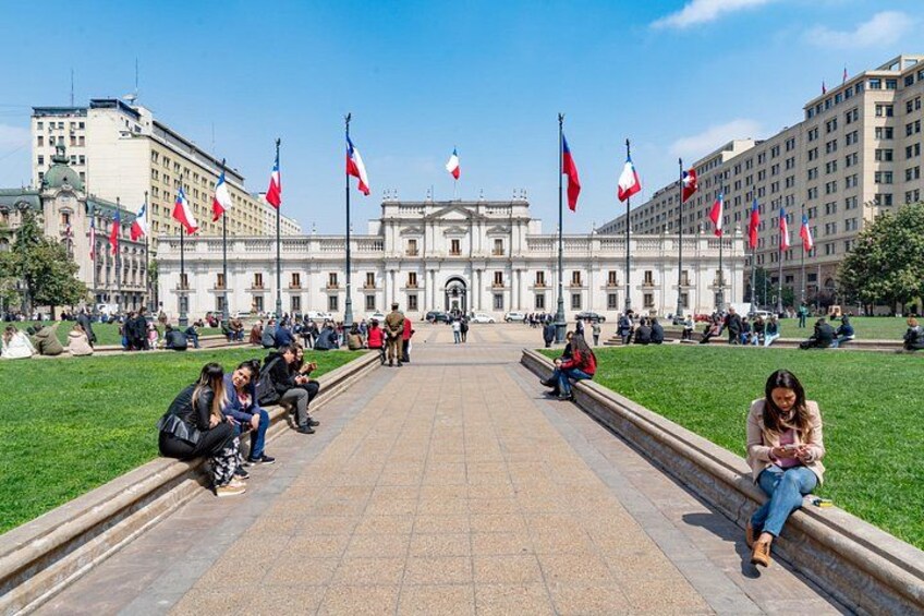Un grand bâtiment orné de nombreux drapeaux, avec un chemin central et des personnes assises sur l’herbe. 1