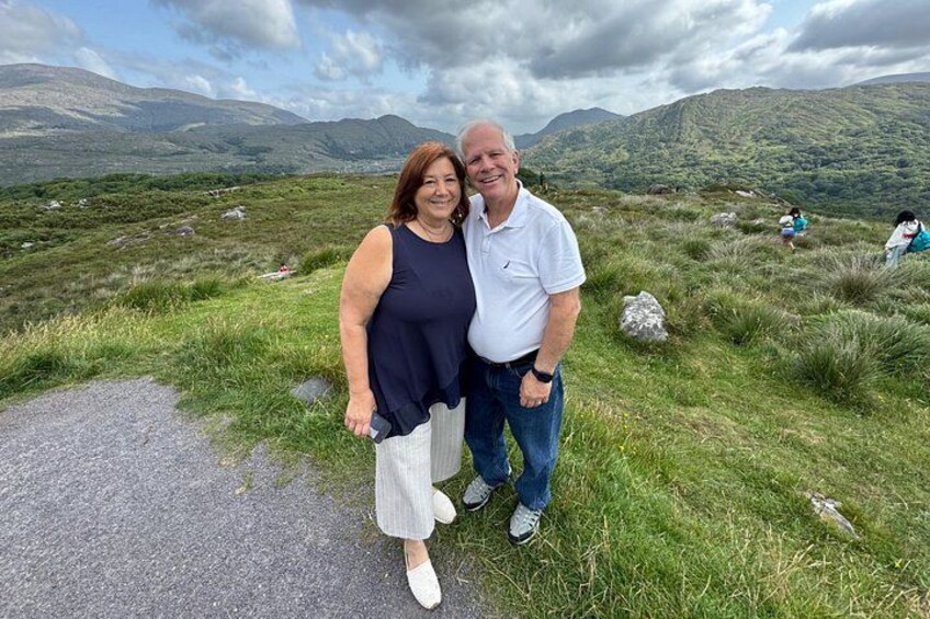 Deux personnes se tiennent sur une colline herbeuse, avec un paysage montagneux en arrière-plan. 2