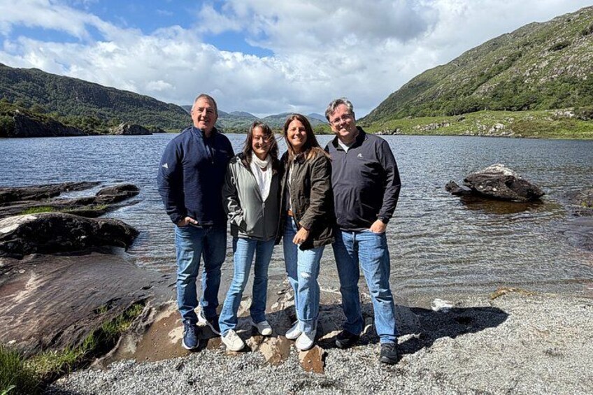 Un groupe de personnes se tient près d’un lac, avec des montagnes en arrière-plan. 1