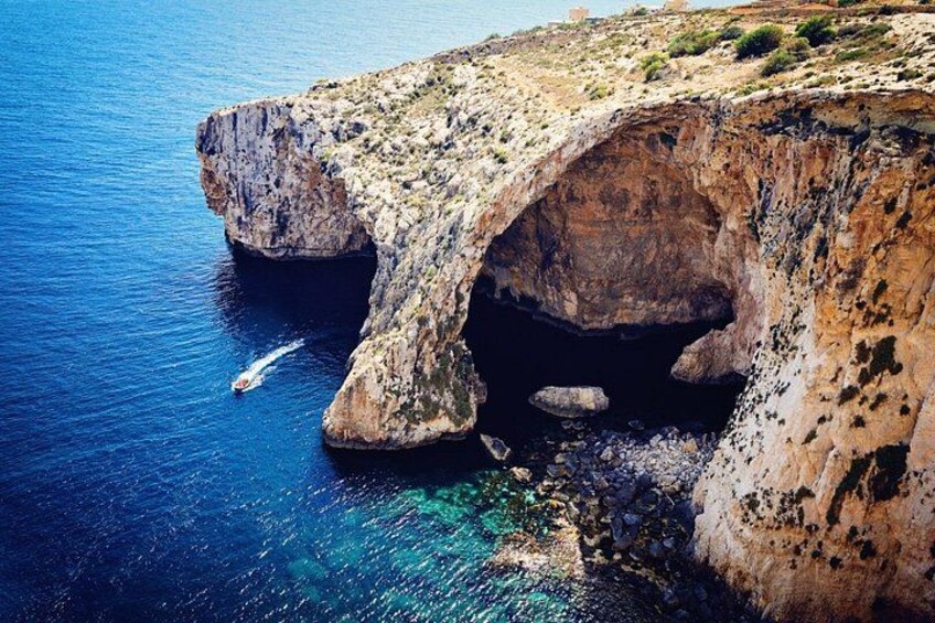 A coastal cliff with a natural arch formation and clear blue waters. 1
