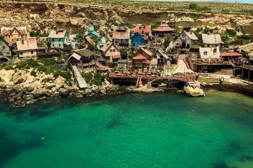 Un pueblo costero con casas construidas sobre pilotes sobre el agua, un puente que conecta el pueblo con tierra firme y una costa rocosa. 4