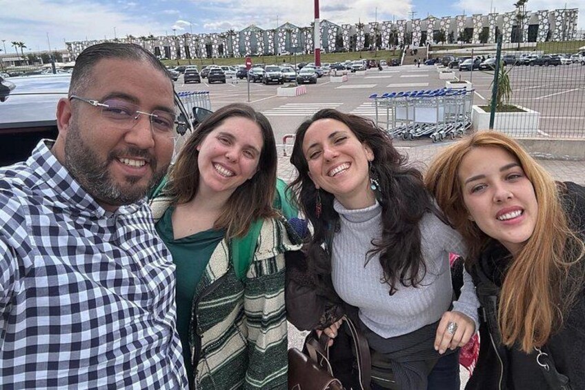 En gruppe mennesker poserer til et foto udendørs med en parkeringsplads og bygninger i baggrunden. 3