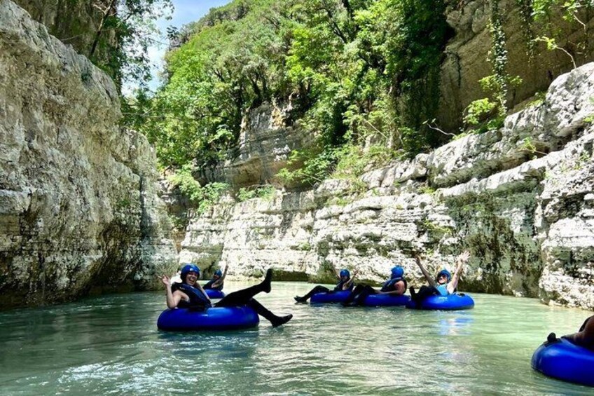 People rafting on blue inflatable tubes in a river surrounded by rocky cliffs and greenery. 2