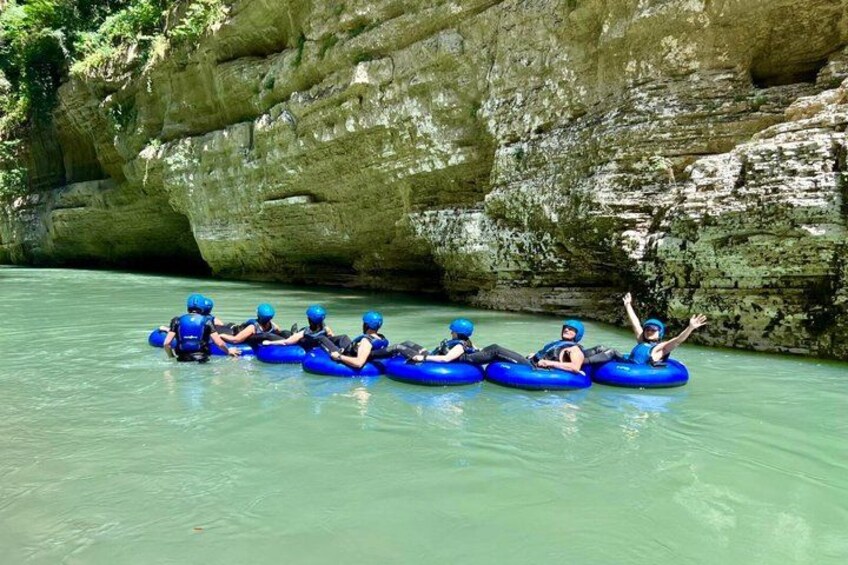 People rafting on a calm river surrounded by rocky cliffs. 3