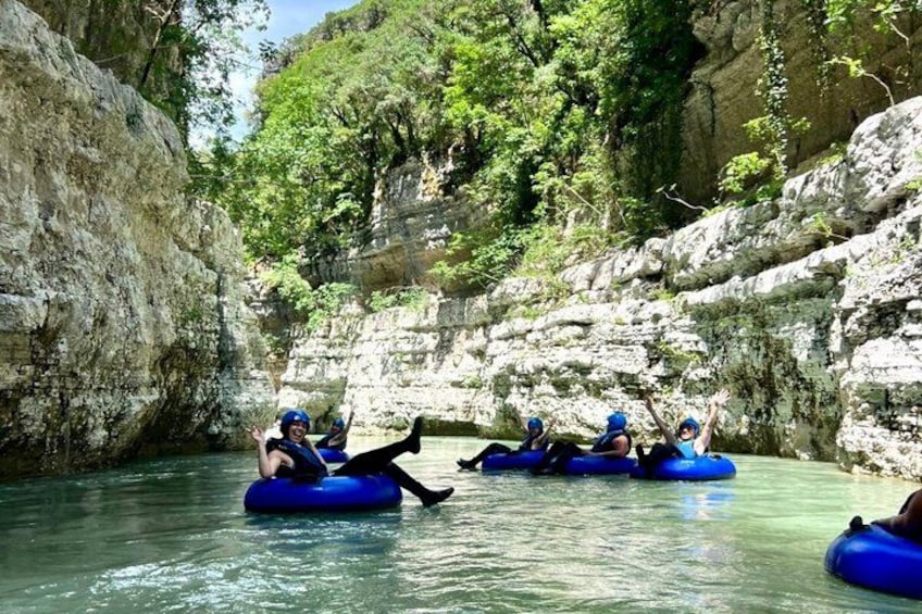People rafting on blue inflatable tubes in a river surrounded by rocky cliffs and greenery. 2