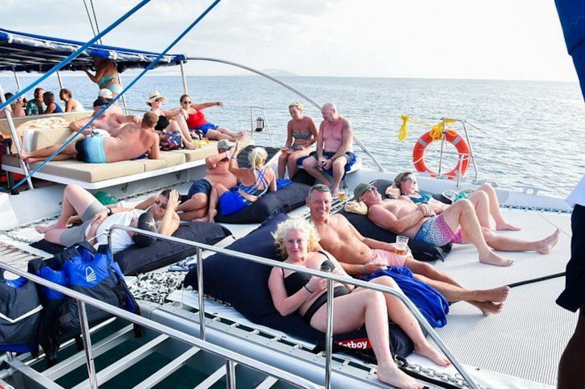 Mensen ontspannen op het dek van een boot, met een reddingsboei en een persoon die staat. 3