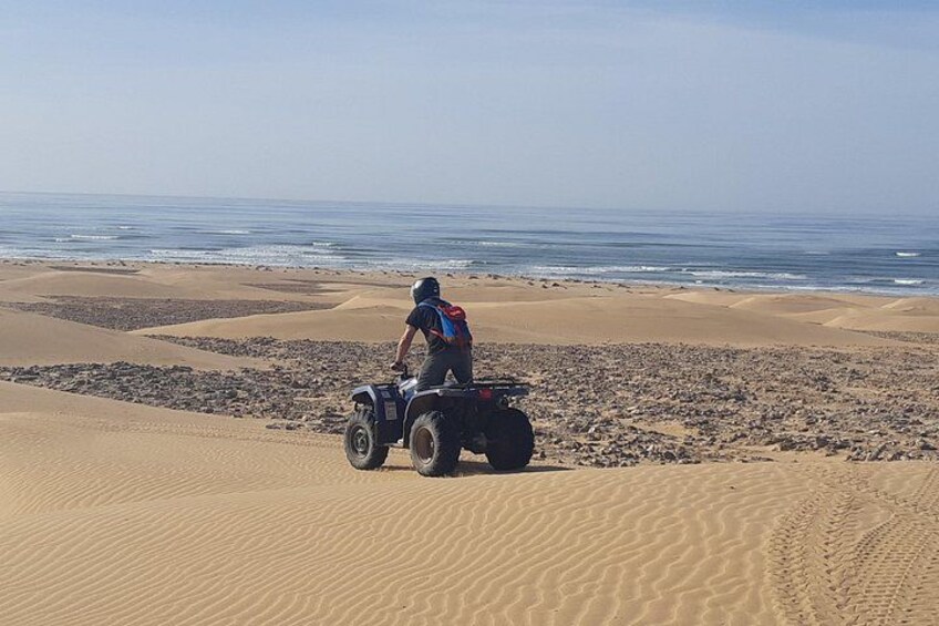Una persona conduciendo un cuatrimoto sobre una playa arenosa con el océano al fondo. 1