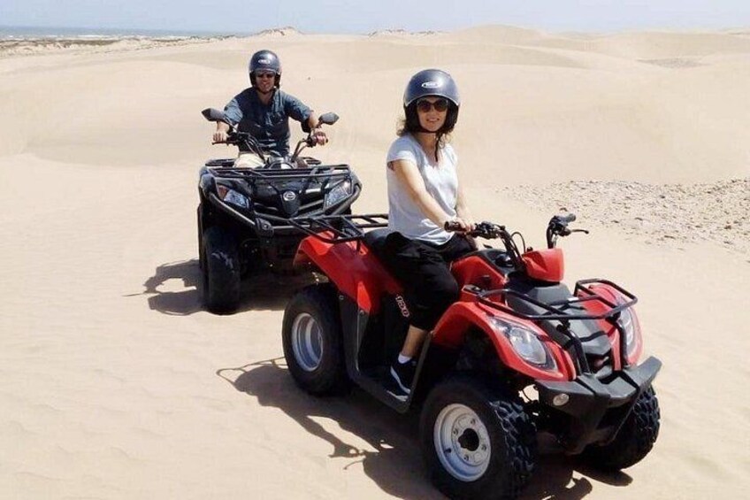 Dos personas en cuatrimotos en un desierto con dunas de arena al fondo. 4
