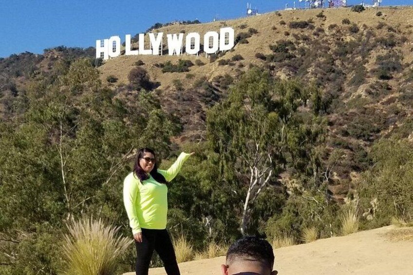 Een persoon staat voor het Hollywood-bordje, met een glooiend landschap op de achtergrond. 2