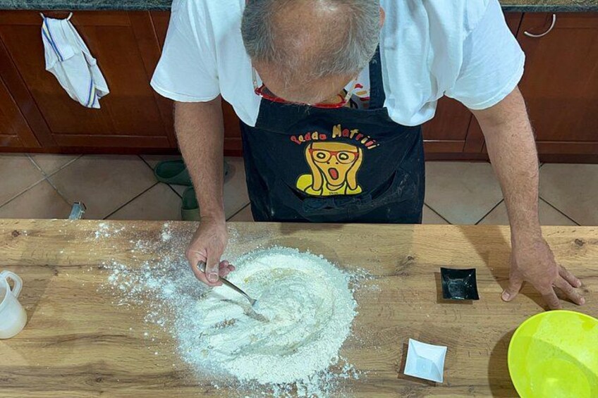 Una persona en una cocina, usando un delantal negro con un personaje de dibujos animados, mezclando ingredientes sobre una tabla de cortar de madera. 4