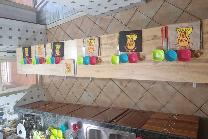 Een keuken met een houten rek vol kleurrijke mokken en een houten plankje met ingelijste foto's. 4