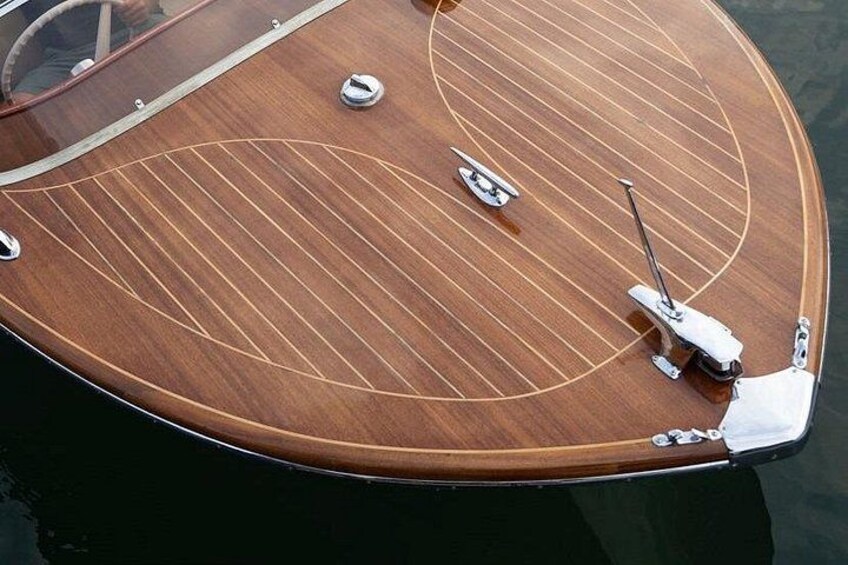 A wooden boat with a circular deck, metal railings, and a white cover on the bow. 1