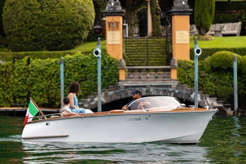 A white boat with 'LAKE TOUR' written on the side, docked near a well-manicured garden with a fountain and statues. 4