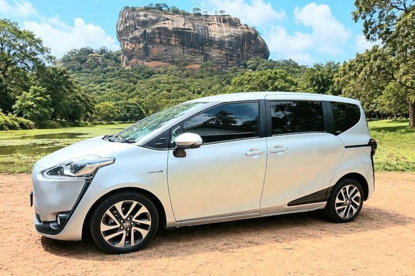 A white car parked on a dirt path with a large rock formation in the background. 3