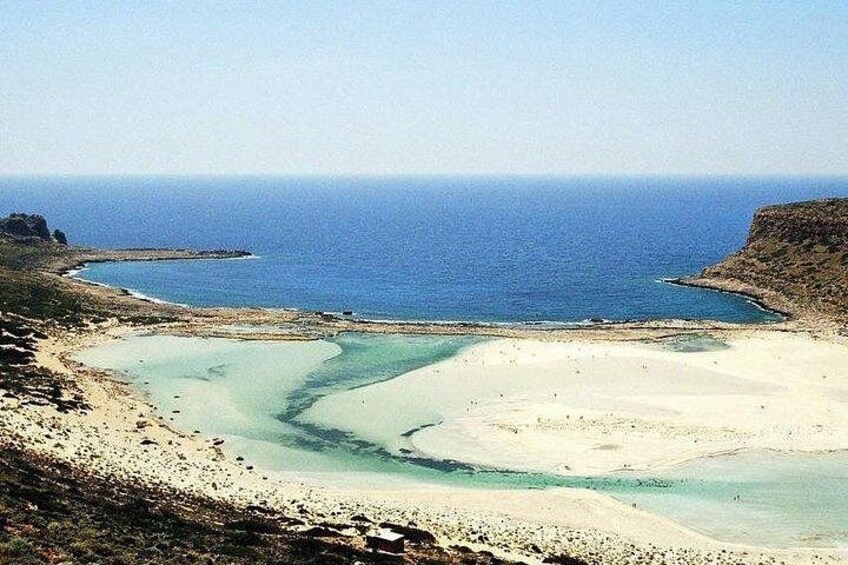 A coastal landscape with a sandy beach, clear blue waters, and a rocky outcrop. 2