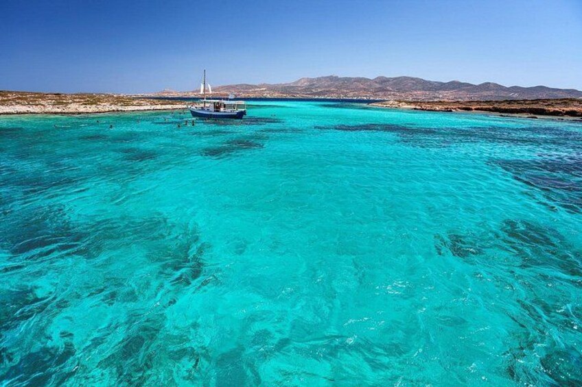 Un barco en un mar turquesa, cielo despejado y montañas a lo lejos. 4
