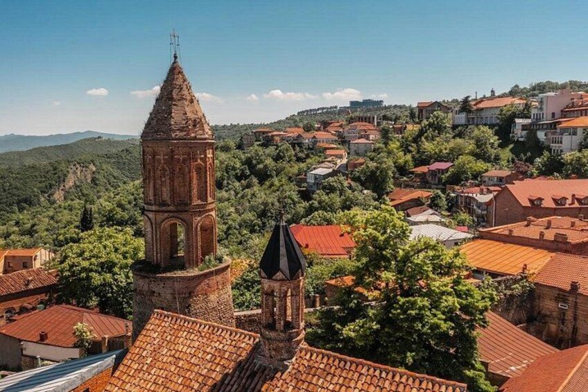 A town with a prominent church tower, red-roofed buildings, and a hilly landscape. 2