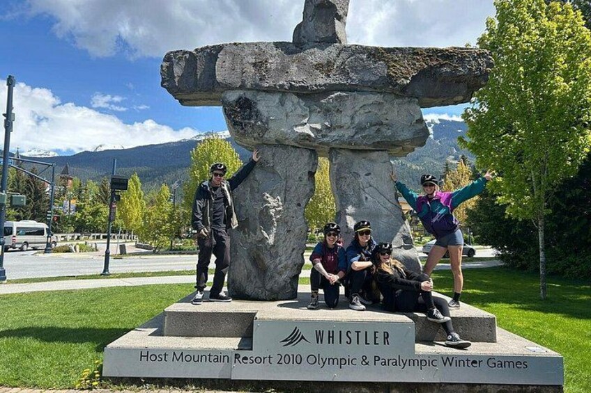 A stone monument with the inscription 'WHISTLER Host Mountain Resort 2010 Olympic & Paralympic Winter Games' and a group of people posing around it. 2