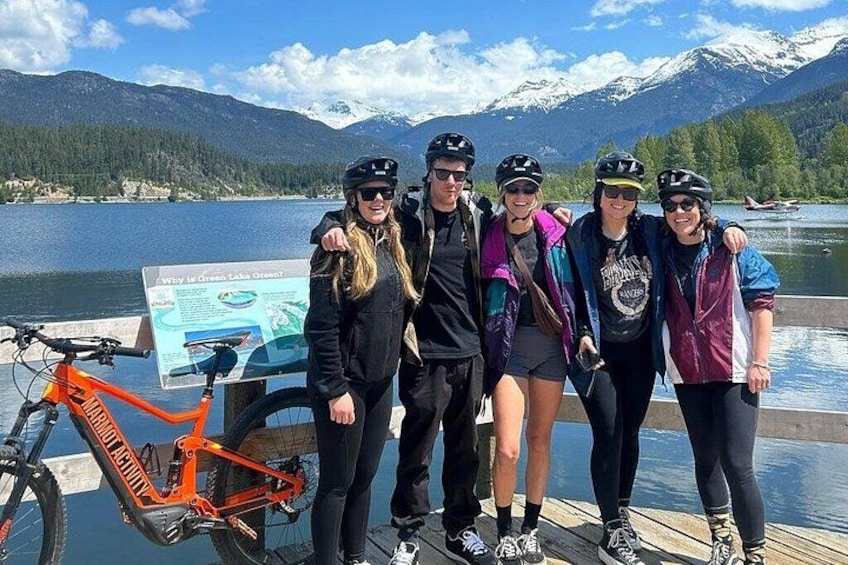 En gruppe mennesker poserer ved en sø med bjerge i baggrunden. 4