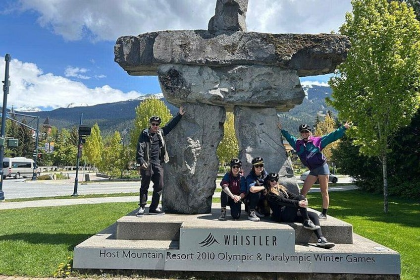 Et stensøjle med indskriften 'WHISTLER Host Mountain Resort 2010 Olympic & Paralympic Winter Games' og en gruppe mennesker, der poserer omkring den. 5