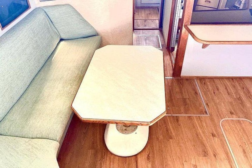 Ett sexkantigt bord med en rund fot, en soffa i ljusa färger och ett trägolv. 2
