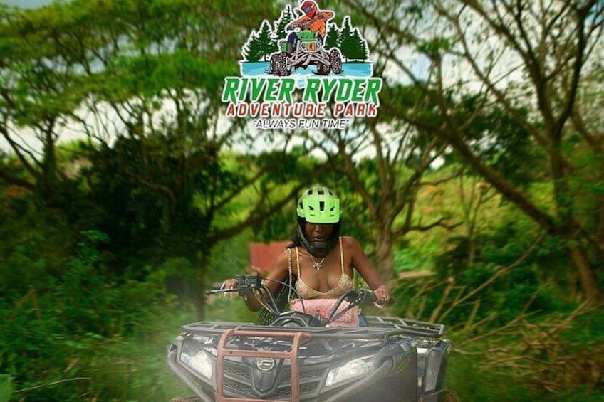 Eine Person fährt mit einem Geländewagen durch ein bewaldetes Gebiet, mit dem Logo des River Ryder Adventure Park. 2