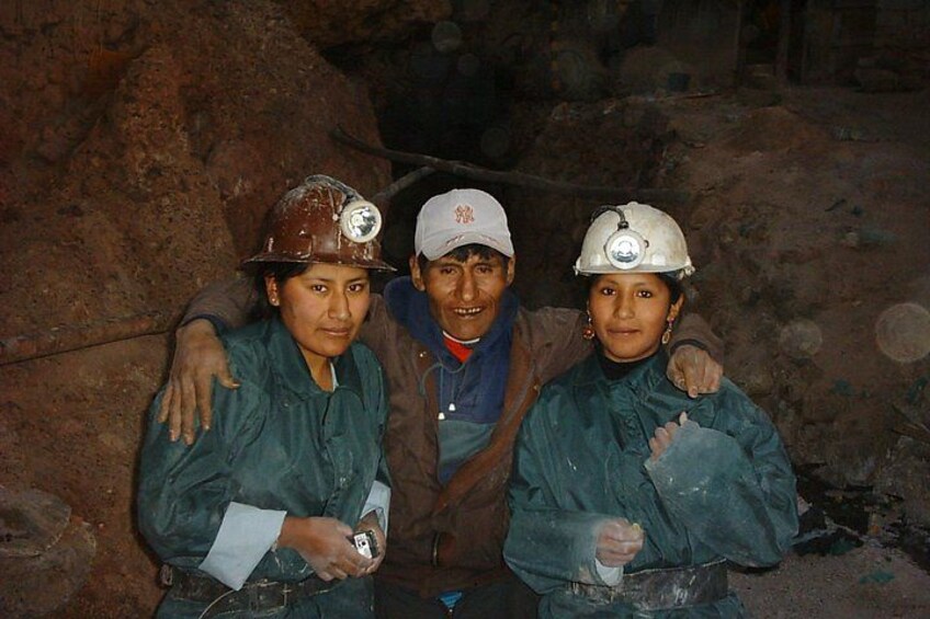 Three people in mining attire with helmets, standing in a rocky, dimly lit environment. 5