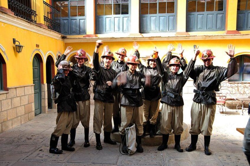 A group of people in uniform with raised hands, standing in a courtyard with yellow walls and blue shutters. 3